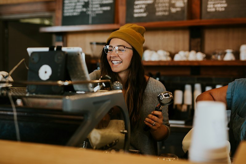 Une commerçante souriante tient un porte-filtre dans son café